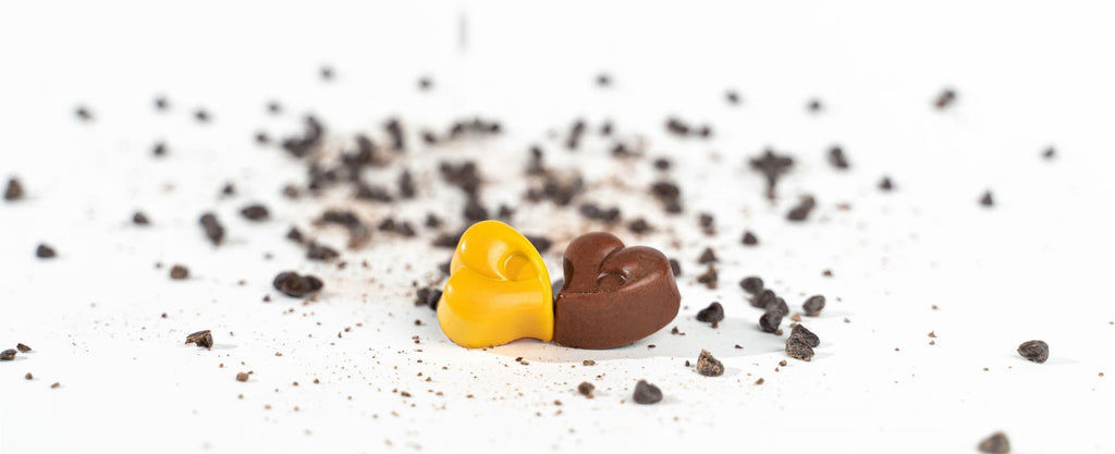 heart shaped chocolate on a white background with scattered cocoa nibs